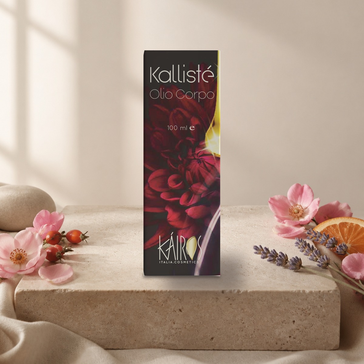 astuccio Kallisté Olio Corpo di Kairos Italia su un blocco di pietra tra fiori rosa, lavanda e fetta di arancia